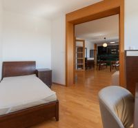 Zariadený 4-izbový byt s balkónmi a parkovaním - Spálňa s posteľou a komodou, spojená s kuchyňou, podlaha s dreveným dekorom.