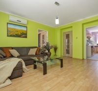 Veľký klimatizovaný 2izbový byt centrum I, Nové Mesto nad Váhom - Obývacia izba s rohovou pohovkou, skleneným stolíkom a podlahou s dreveným dekorom.