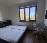 Bývanie pod Tatrami: 3-izbový apartmán v Starej Lesnej - Spálňa s posteľou, stolom a podlahou s dreveným dekorom v 3-izbovom byte.