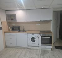 Moderný prenájom na ulici Bakossova za 550 € mesačne - Kuchyňa v 1-izbovom byte s bielou kuchynskou linkou a podlahou s dreveným dekorom.