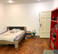 Prenájom 2 izbový byt, Murgašova ulica, Bratislava I. Staré Mesto - Spálňa s posteľou, červenou policou a podlahou s dreveným dekorom v 2-izbovom byte.
