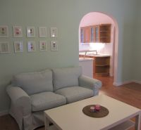 4-izb.byt v centre mesta, Obchodná ul., BA I - Staré Mesto, 2 x balkón - Obývačka 4-izbového bytu s pohovkou, stolíkom a kuchynským kútom, podlaha s dreveným dekorom.