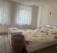 NA PREDAJ celoročná chata – Sekule (Šutrovňa), tiché prostredie - Spálňa v chate s posteľou, kobercom, bielou komodou a závesmi, podlaha s dreveným dekorom.