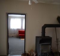 Domček na chalupárčenie s veľkým pozemkom s termál kúpaliskom v obci! - V Rodinnom dome je stropný ventilátor, kachle a červený gauč v pozadí.