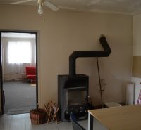 Domček na chalupárčenie s veľkým pozemkom s termál kúpaliskom v obci! - Interiér rodinného domu s krbom, ventilátorom a červenou sedačkou v pozadí.