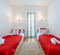 Brač(HR) - Apartmány v 1. rade u mora !!! - Rekreačný apartmán s dvomi posteľami, červenou prikrývkou a podlahou s dreveným dekorom.