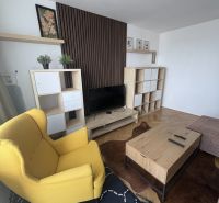 Prenájom 2i-byt s lodžiou s krásnym výhľadom na Račianskej ulici - Obývacia izba s podlahou s dreveným dekorom, žltým kreslom a dreveným konferenčným stolíkom.