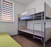 ŠTÝLOVÝ 3-IZBOVÝ BUNGALOV V KÚPEĽNÝCH DUDINCIACH - Poschodová posteľ a zelený gauč v rodinnom dome s podlahou s dreveným dekorom.