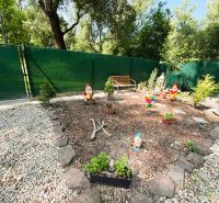 Celoročne obývateľná chata v Gabčíkove na 150 m² pozemku pri Dunaji - Záhrada s trpaslíkmi a lavičkou pri chate v Gabčíkove, obkolesená kameňmi a plotom.