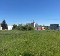 LUKRATÍVNY SP V BUDMERICIACH NA VÝSTAVBU RD ALEBO  BYT.DOMOV - 4459 m2 - Pozemky - bývanie na J.Rašu v Budmericiach, trávnatá plocha, budovy v pozadí.