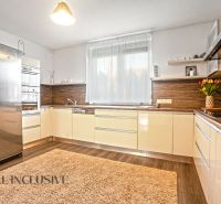 NA PREDAJ 4-IZBOVÝ RODINNÝ DOM V TOMÁŠIKOVE - Kuchyňa v rodinnom dome s béžovým nábytkom, veľkou chladničkou a podlahou s dreveným dekorom.