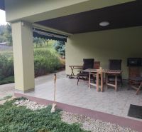  Priestranný dom v Trebostove  - Terasa rodinného domu v Trebostove s dreveným záhradným nábytkom a upravenou zeleňou.