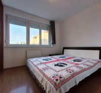 | priestranný | 2i byt s balkónom | parkovaním | Koprivnická - Spálňa v 2-izbovom byte s podlahou s dreveným dekorom a veľkým oknom.