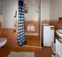 Perspektívny 3 izbový byt RUŽOMBEROK - Kúpeľňa v 3-izbovom byte s oranžovými obkladačkami, sprchovacím kútom, práčkou a WC.