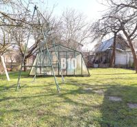 Veľký rodinný dom Turany - Záhrada rodinného domu v Turanoch s hojdačkou a skleníkom, obklopená stromami.