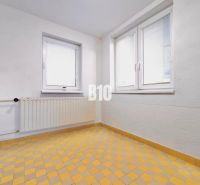 Rodinný dom s rovinatým 10a pozemkom - Biela stena, okná, radiator a žltá kachľová podlaha v rodinnom dome.