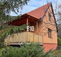 Priestranný rodinný dom s garážou na veľkom pozemku v obci Vlkas - Rodinný dom vo Vlkase obklopený zeleňou, tradične šikmá strecha, drevený balkón.