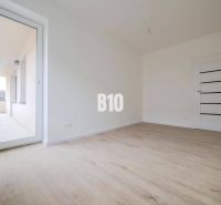 Novostavba -3 izbový byt neďaleko Trenčína - Izba s podlahou s dreveným dekorom a veľkými dverami na balkón v 3-izbovom byte.