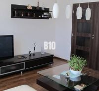 Priestranný 4 izbový byt - Solinky - Obývačka s televízorom, poličkami, stolíkom a podlahou s dreveným dekorom v 4-izbovom byte.