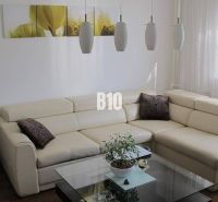 Priestranný 4 izbový byt - Solinky - Elegantná obývacia izba v 4-izbovom byte s krémovou sedačkou a podlahou s dreveným dekorom.