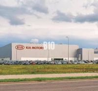 V  PRIAMEJ BLÍZKOSTI KIA  11000m2 lukratívny pozemok na výstavbu - Budova Kia Motors v Žiline, pozemky - komerčné so zaparkovanými autami a trávnatou plochou.