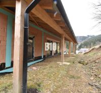 Nová, stavba rodinného domu pri lyžiarskom stredisku - Trenčiansky kra - Rodinný dom vo výstavbe s dreveným prístreškom, rovným terénom a okolitou krajinou.