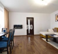 3-izbový byt s parkovaním vo dvore - Obývacia izba v 3-izbovom byte s podlahou s dreveným dekorom, sedačkou a jedálenským stolom.