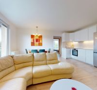 | Pekný a priestranný 3-izbový byt | 70m² |  - Obývacia izba 3-izbového bytu s podlahou s dreveným dekorom, kuchyňou a balkónom.