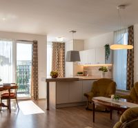Moderný 2-izbový apartmán s parkovaním, Vila Leonardo, Bajkalská - Obývačka v 2-izbovom byte s podlahou s dreveným dekorom a svetlou kuchyňou.