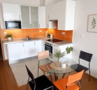 Garsonka 35m2, balkón,novostavba, Sliačska ul. Energie v cene. - Kuchyňa v garsónke s bielou linkou, oranžovým obkladom a okrúhlym stolom s dreveným dekorom.