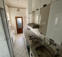 Byt na rekonštrukciu v centre Bratislavy – výborný projekt - Kuchyňa v 2-izbovom byte s bielymi skrinkami a dlažbou na podlahe.
