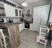 2 izbovy byt s balkónom Topoľčany  - Kuchyňa v 2-izbovom byte s bielym nábytkom, barovým pultom a podlahou s dreveným dekorom.