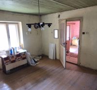 Na predaj vidiecky dom v Dedinke 3+1 s pozemkom 3150m2  - Izba v rodinnom dome s podlahou s dreveným dekorom, starší nábytok a okno.
