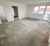 Na predaj 3 izb. byt s balkónom blízko centra - Izba v 3-izbovom byte, biele steny, veľké okno a surová podlaha.