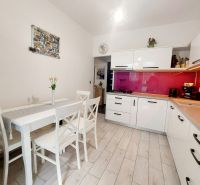NOVÁ CENA-NA PREDAJ  pekný 3ibyt Prievidza-Necpaly - Kuchyňa v 3-izbovom byte s bielymi skrinkami, ružovým obkladom a podlahou s dreveným dekorom.