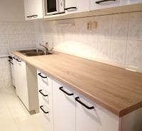 PRENÁJOM: ÚTULNÝ 2 IZBOVÝ BYT S BALKÓNOM, UHLISKO - Kuchyňa v 2-izbovom byte s bielymi skrinkami a podlahou s dreveným dekorom.