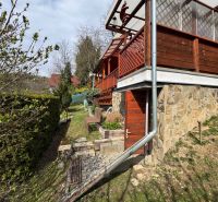 PREDAJ Rekreačná chata so záhradkou, Suchá Dolina, Košice-Sever - Chata v Svinici s kamennou fasádou a drevenou terasou, obklopená zeleňou.