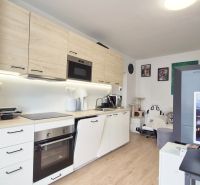 JEDNOIZBOVÝ PREROBENÝ NA DVOJIZBOVÝ BYT - Kuchyňa v 2-izbovom byte s bielymi skriňami, podlahou s dreveným dekorom a dekoráciami na stene.