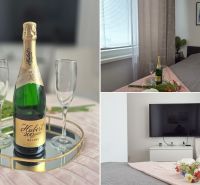 MODERNÝ DVOJIZBOVÝ BYT, 37M2, DÚBRAVKA - 2-izbový byt s posteľou, šampanským, dvoma pohármi a TV na stene.