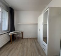 Na predaj 1-izbový byt s loggiou - Žiar nad Hronom, M. Chrasteka 1B718 - Jednoduchá izba s písacím stolom, skriňou a podlahou s dreveným dekorom v 1-izbovom byte.
