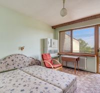 6-izbový rodinný dom v obci Biely Kostol - Spálňa v rodinnom dome s výhľadom na balkón, kvietkované posteľné čelo, stolička, stôl.