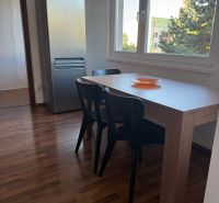 Prenájom 3-izb. byt Ku Bratke - zariadený - Jedálenský kút s tromi stoličkami a stolom, vedľa chladničky, podlaha s dreveným dekorom.