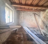 Na predaj vidiecky rodinný dom - Žarnovica/Brehy D045ZL - Izba v rodinnom dome s kamennými stenami a dreveným stropom, materiál na podlahe.
