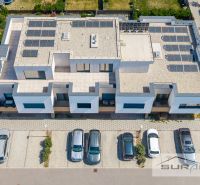 Nový 3-izbový byt 82 m² | Terasa 97 m² | Mesačná ulica | Hviezdoslavov - Budova na Mesačnej ulici v Hviezdoslavove so solárnymi panelmi a zaparkovanými autami.