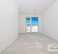 Nový 3-izbový byt 82 m² | Terasa 97 m² | Mesačná ulica | Hviezdoslavov - Prázdna miestnosť s betónovou podlahou a balkónovými dverami v 3-izbovom byte.