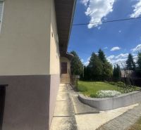 Rodinný dom Orlov - na predaj  - Rodinný dom v Orlove s chodníkom a zeleňou, obkolesený stromy a modrou oblohou.