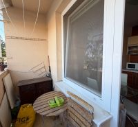 3 izbový byt s balkónom v meste Levice - Balkón 3-izbového bytu s dreveným stolom a stoličkami, vedľa kuchynského okna.