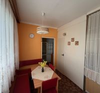 2 izbový byt pri vlakovej stanici v Nových Zámkoch - Kuchyňa v 2-izbovom byte s oranžovou stenou, koberec a čipkované záclony.