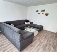 Tehlový 2-izbový byt s vlastným kúrením vo Vrbovom - Obývačka s rohovou sedačkou, skleneným stolíkom a podlahou s dreveným dekorom.