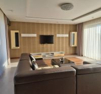 PRENÁJOM- Jedinečný, luxusný byt 148 m2 s terasami a parkovaním -Nitra - Obývacia izba s hnedou sedačkou, televízorom na stene a veľkými oknami. Idealne pre 4-izbový byt na ulici Dolnohorská.